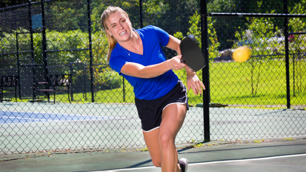 Woman playing PICKLEBALL in outdoor court.