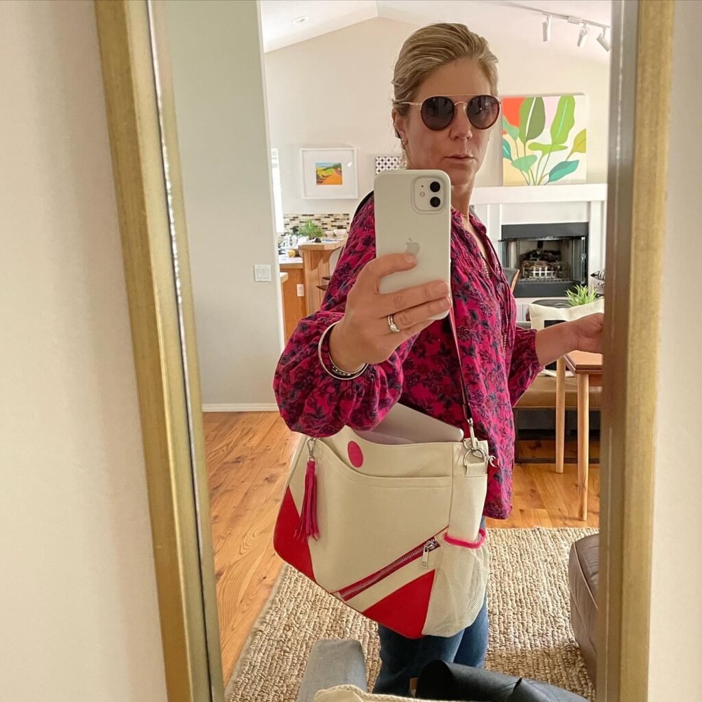 Woman taking mirror selfie with stylish pink shirt and sunglasses.